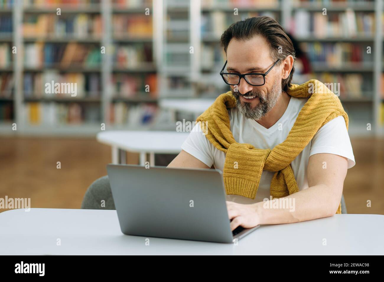 Glückliche Freiberufler mittleren Alters verwendet Laptop, chatten mit Kollegen, sitzen am Schreibtisch. Joyful stilvolle Mann arbeitet an neuen Business-Plan für Unternehmen, Projekt zu entwickeln Stockfoto