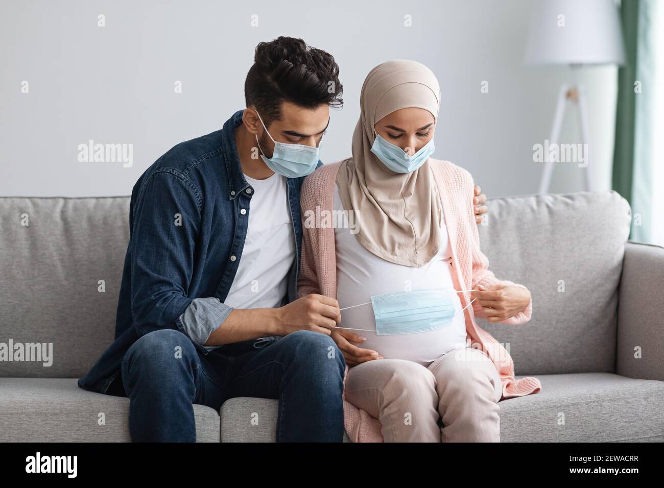 Coronavirus Und Schwangerschaft. Muslimische Ehegatten Setzen Schützende Medizinische Maske Auf Schwangeren Bauch Stockfoto