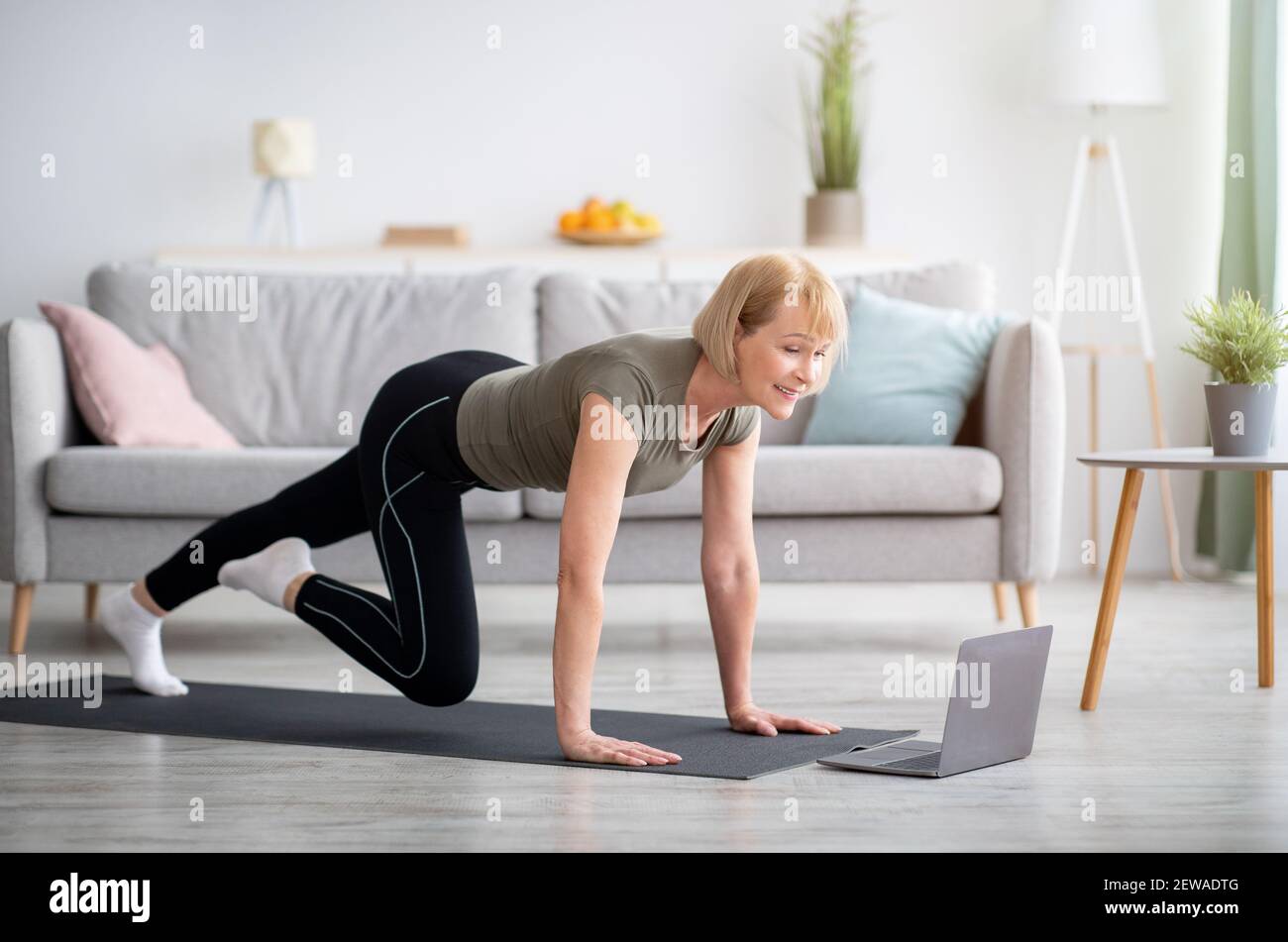 Online-Sport in der Isolation zu Hause. Fit reife Dame macht Übungen vor dem Laptop drinnen, kopieren Platz Stockfoto