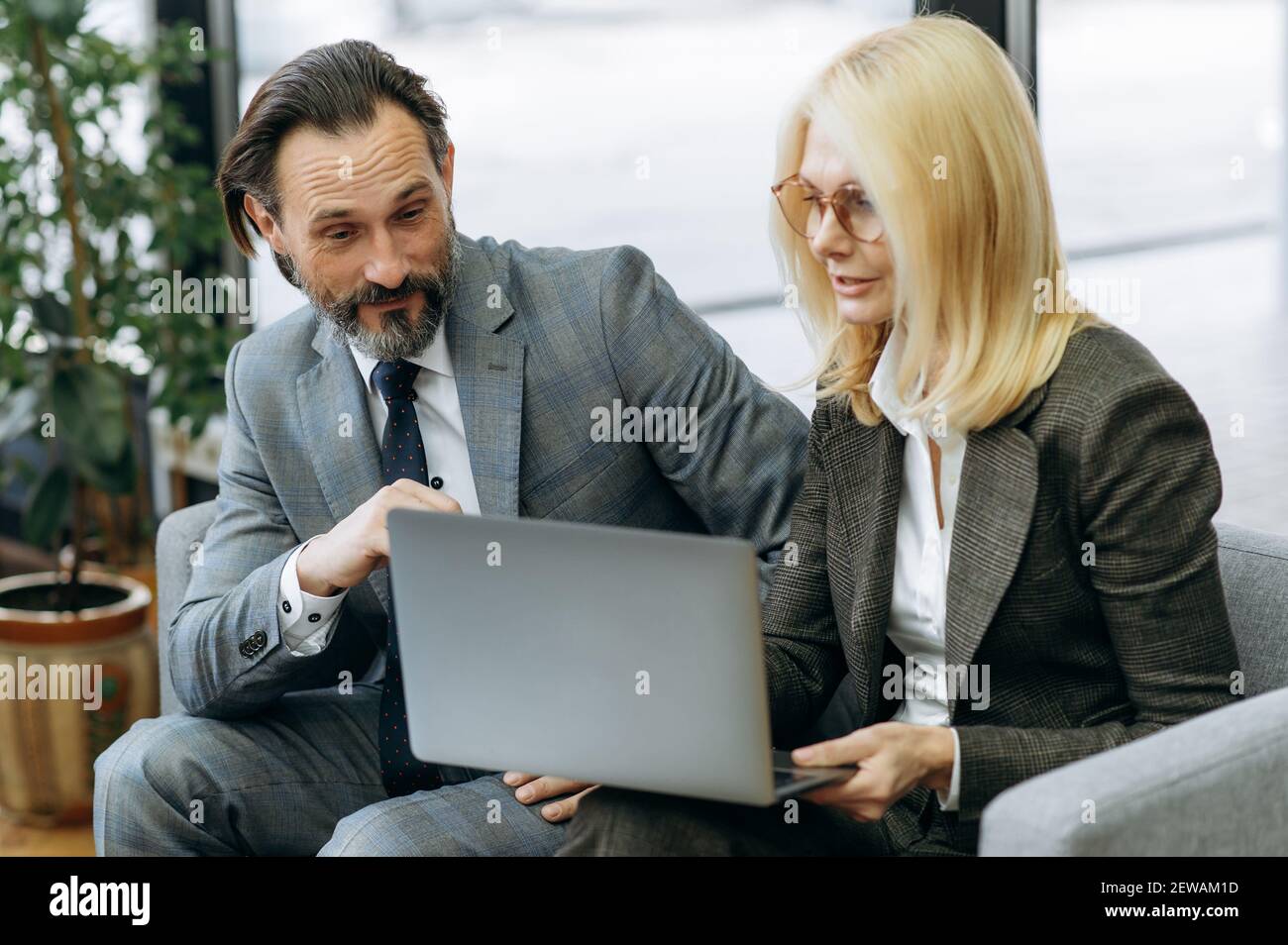 Beschäftigte Büroangestellte sitzen auf dem Sofa, benutzen Laptop, arbeiten zusammen an Projekt. Erfolgreiche Geschäftspartner diskutieren Ideen für Startup, Surfen im Internet, Teamwork-Konzept Stockfoto