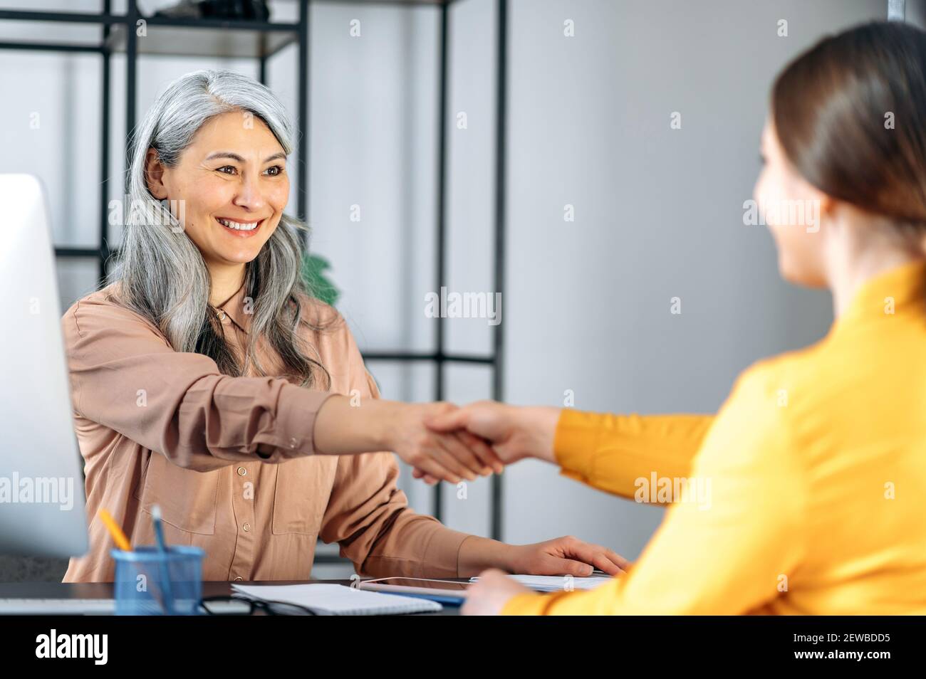 Eine asiatische reife grauhaarige freundliche Geschäftsfrau, schüttelt die Hände mit Frau Arbeitssuchende. Erfolgreiche Dame mittleren Alters macht Deal mit weiblichen Geschäftspartner Stockfoto