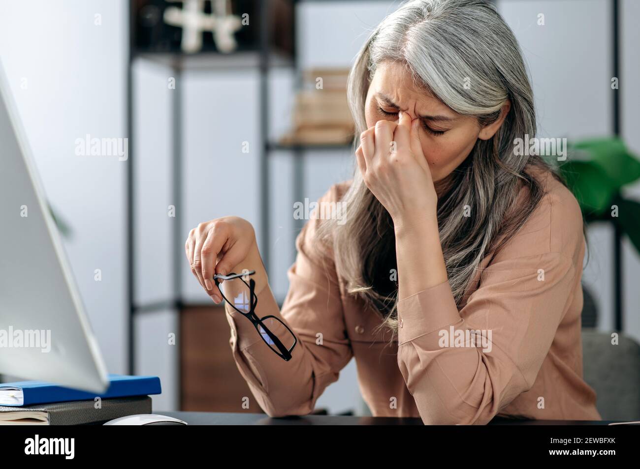 Überfordert müde ältere Dame mit Brille Gefühl Kopfschmerzen, nach der Arbeit am Computer. Traurige reife grauhaarige Ermüdung Frau wird Augen am Arbeitsplatz massiert Stockfoto
