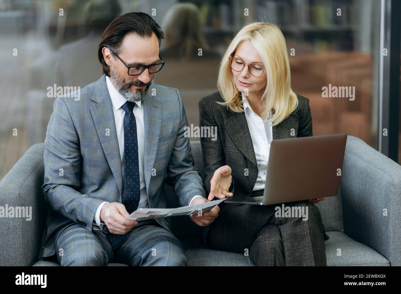 Konzentrierte kaukasische leitende Kollegen arbeiten zusammen an einer neuen Geschäftsstrategie für das Unternehmen. Seriöse männliche und weibliche Mitarbeiter lernen Dokumente, mit Laptop, sitzen auf dem Sofa Stockfoto