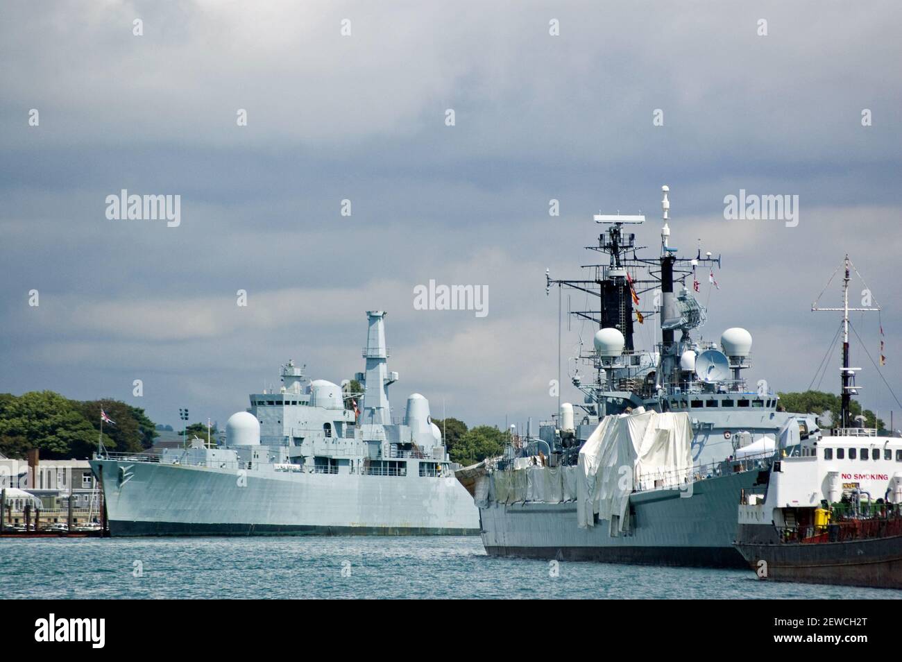 Royal Navy Schiffe in Portsmouth Dockyard, Hampshire. Ein Zerstörer befindet sich auf der linken Seite des Bildes. Stockfoto