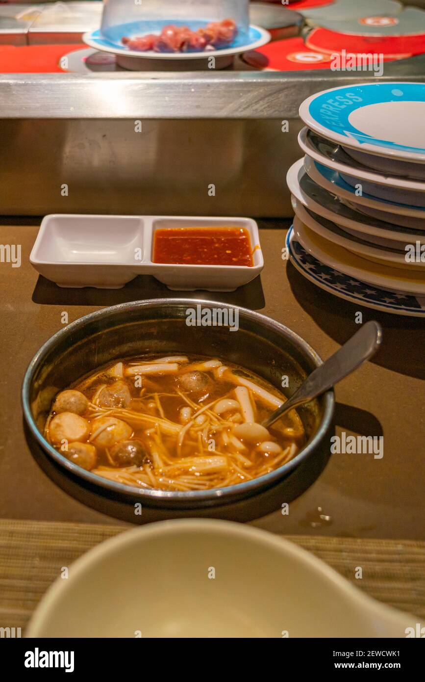 Würzige Enoki-Pilzsuppe im Hotpot-Förderband-Restaurant Stockfoto