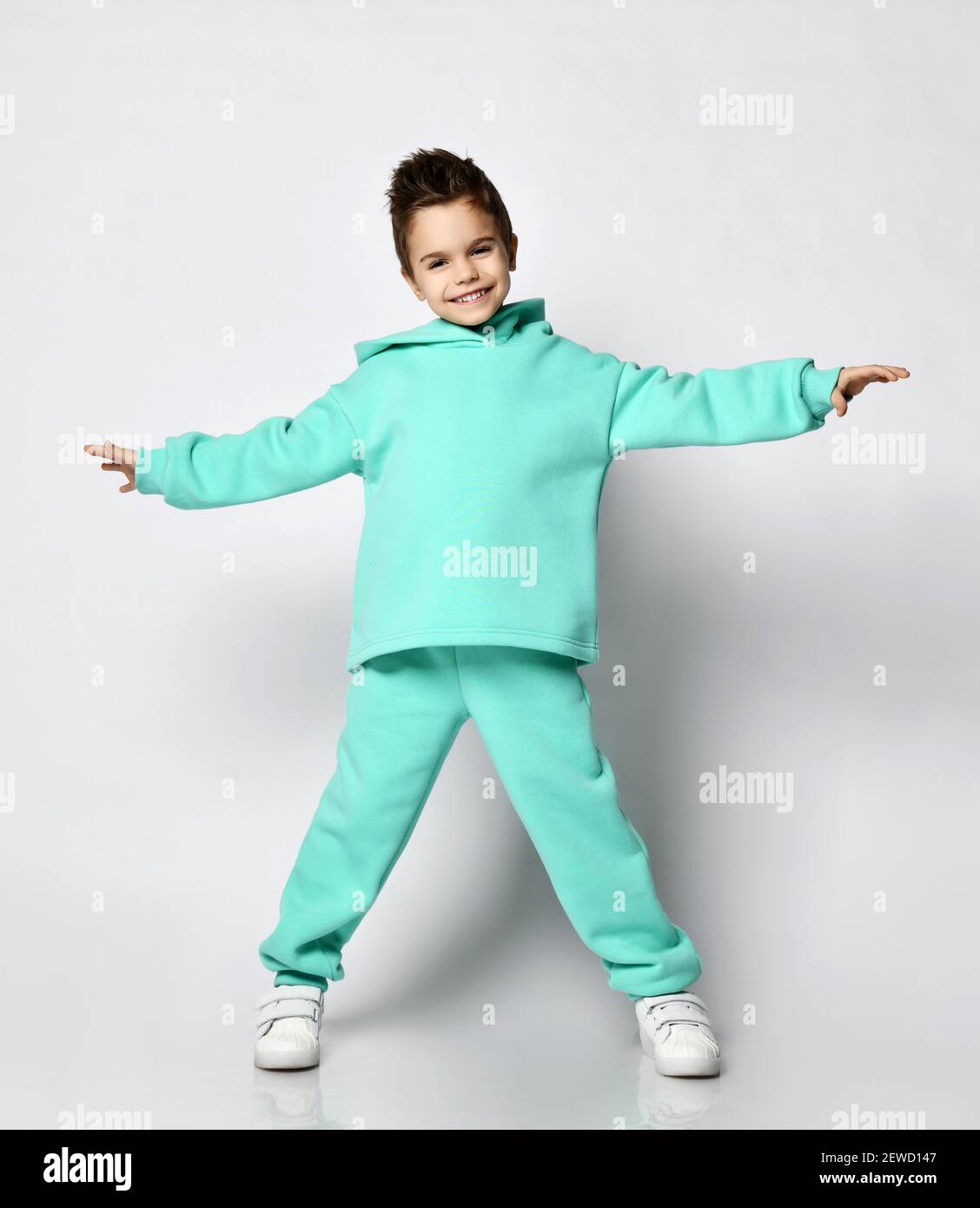 Young Active positive Kid Boy mit stylischem Haarschnitt in modernem Grün, mintfarbenem Kapuzenpullover mit aufgehellten Händen Stockfoto