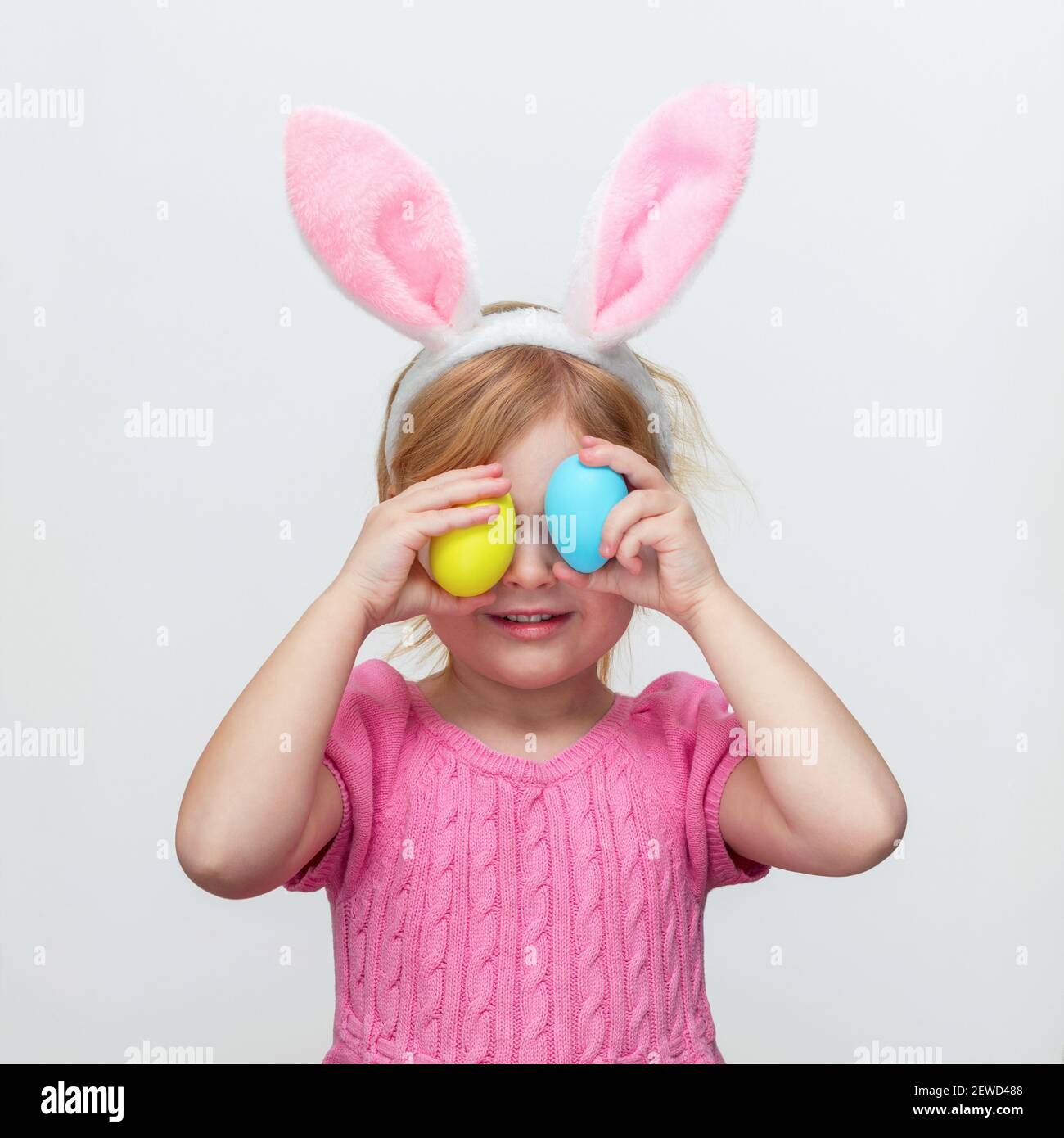 Schönes lächelndes kleines Mädchen trägt Osterhasen Ohren und hält Ostern gefärbte Eier auf weißen Wand Hintergrund. Stockfoto