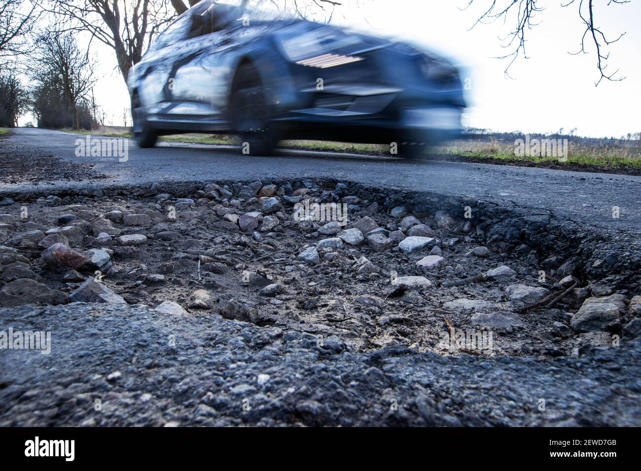 Gottesgabe, Deutschland. Februar 2021, 26th. Ein Auto fährt in einer Allee an einem Schlagloch vorbei. Das eisige Wetter der letzten Wochen sorgt für durchbrochene Straßen mit tiefen Schlaglöchern. Quelle: Jens Büttner/dpa-Zentralbild/dpa/Alamy Live News Stockfoto