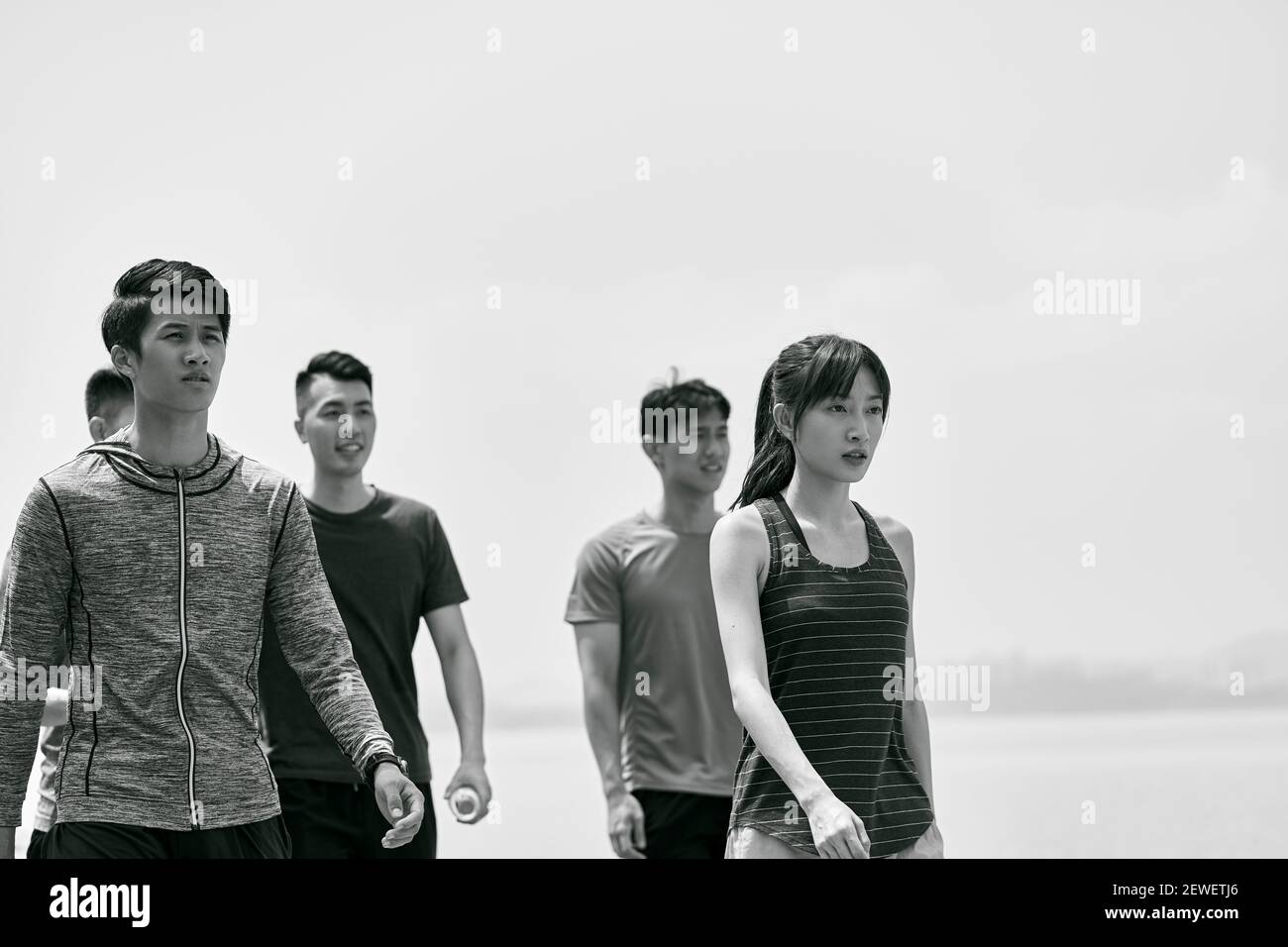 Gruppe von fünf jungen asiatischen Erwachsenen, die nach dem Training im Freien spazieren gehen, schwarz und weiß Stockfoto