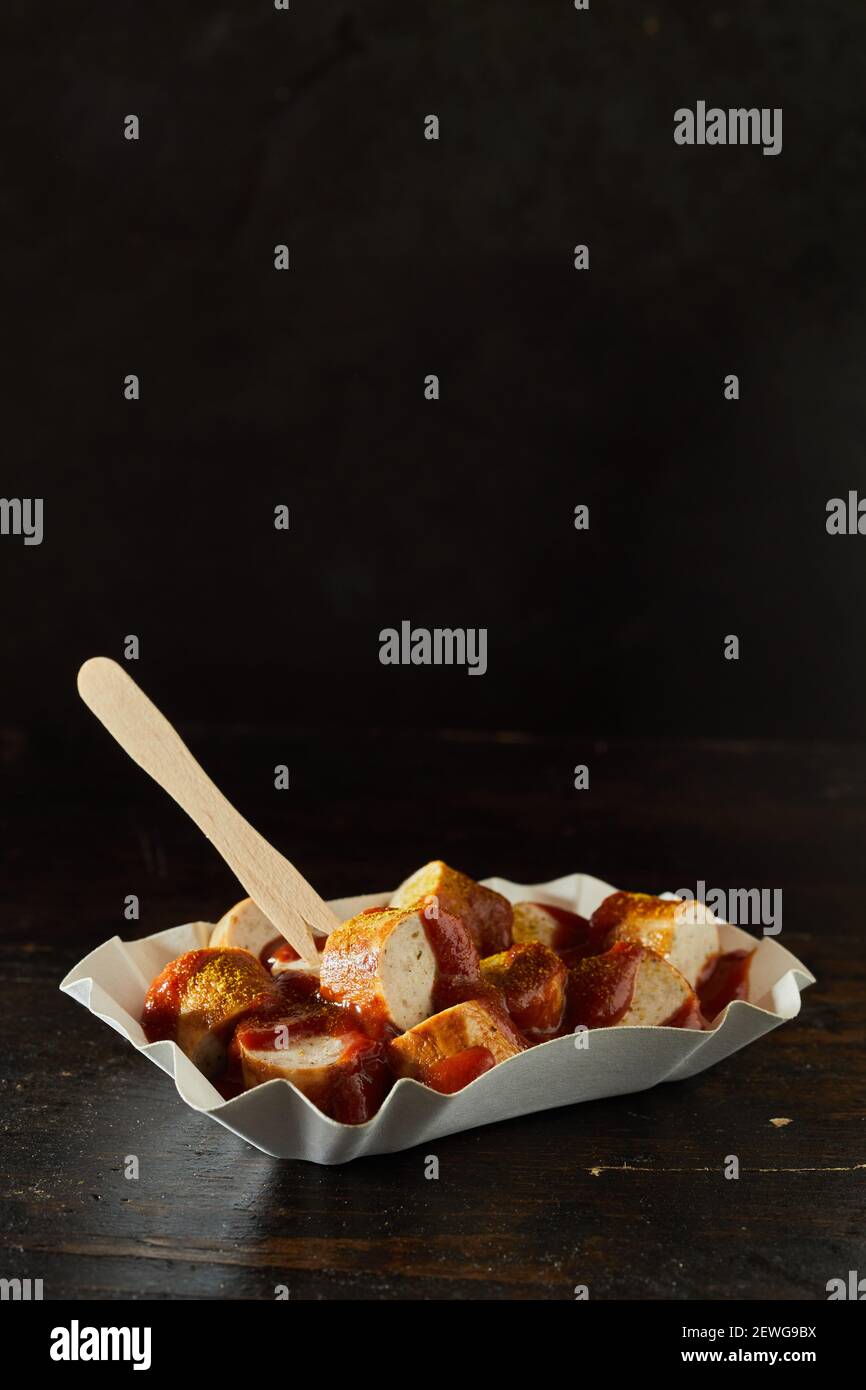 Take-away-Behälter mit leckeren gebratenen Schweinswurst-Brocken bedeckt Ketchup und trockenes Curry Stockfoto