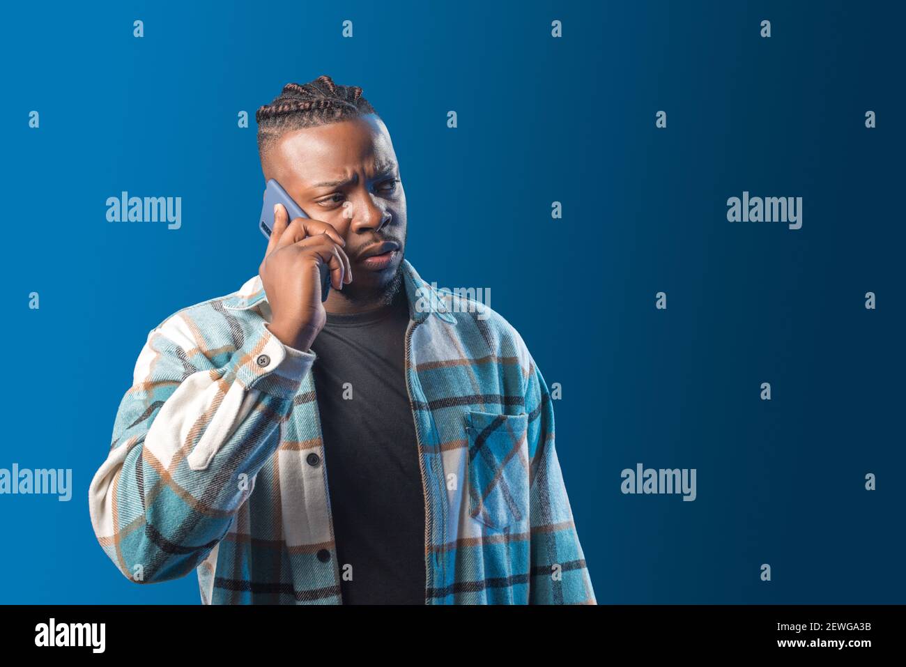 Hübscher schwarzer Mann, der auf dem Handy sprach, sorgte sich. Mittlere Aufnahme. Blauer Hintergrund. Stockfoto