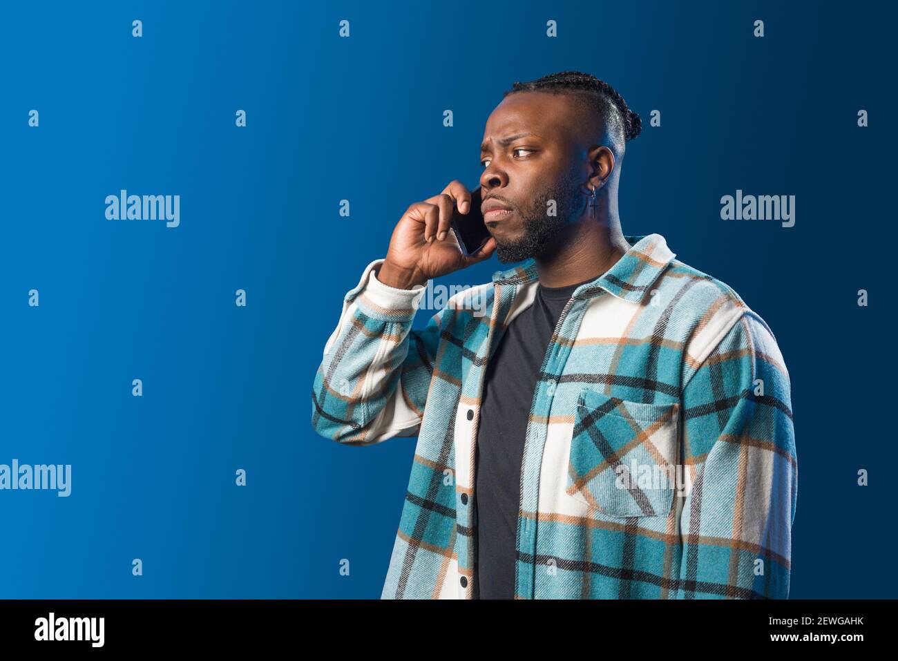 Hübscher schwarzer Mann, der auf dem Handy sprach, sorgte sich. Mittlere Aufnahme. Blauer Hintergrund. Stockfoto