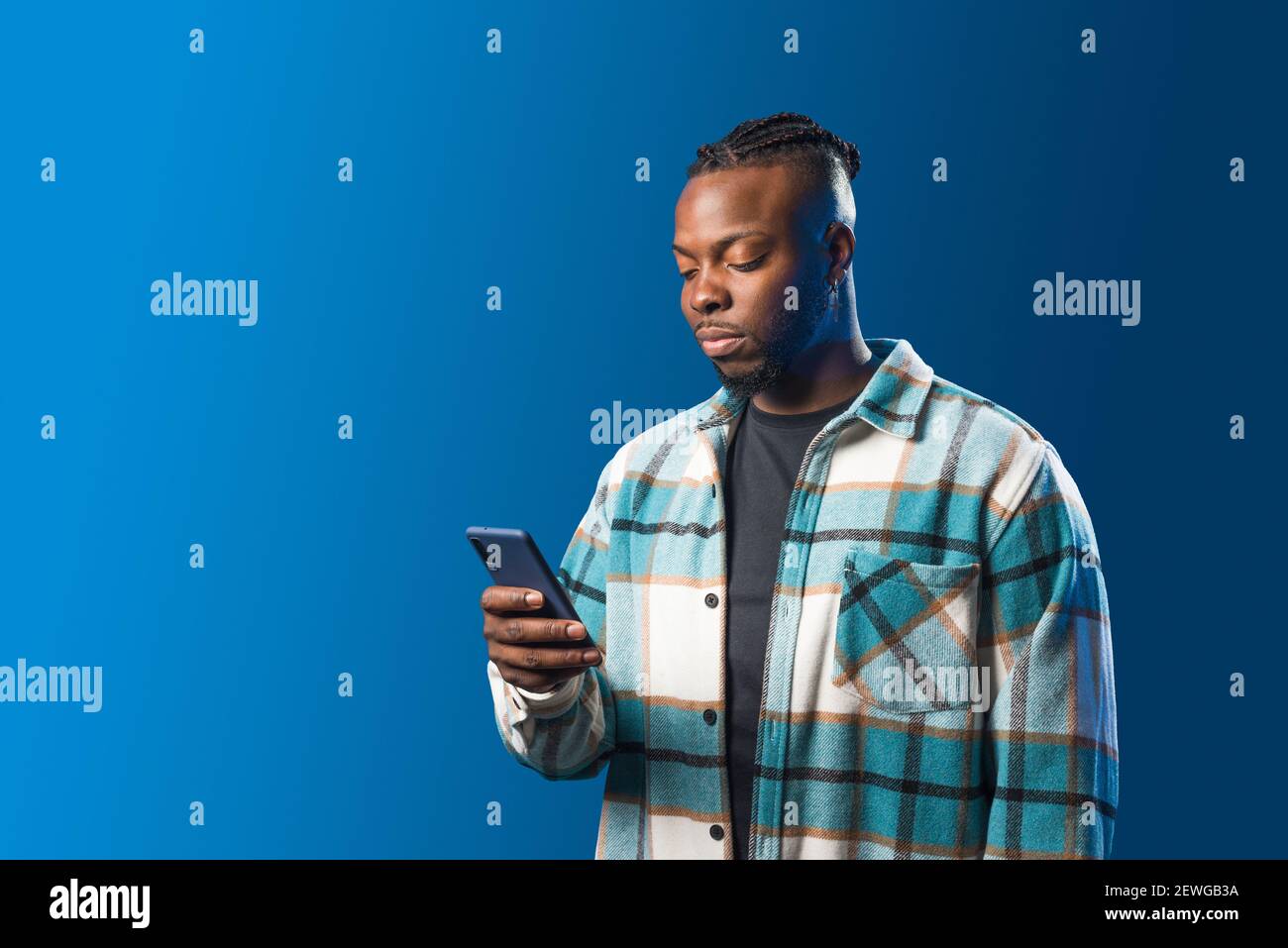 Schöner schwarzer Mann, der auf Handy schaut. Mittlere Aufnahme. Blauer Hintergrund. Stockfoto