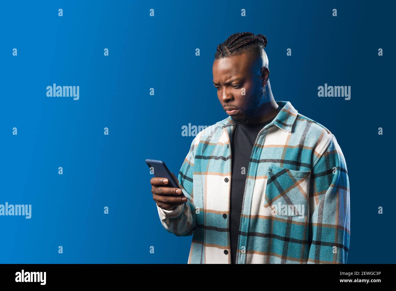 Hübscher schwarzer Mann, der sich Sorgen um das Handy macht. Mittlere Aufnahme. Blauer Hintergrund. Stockfoto