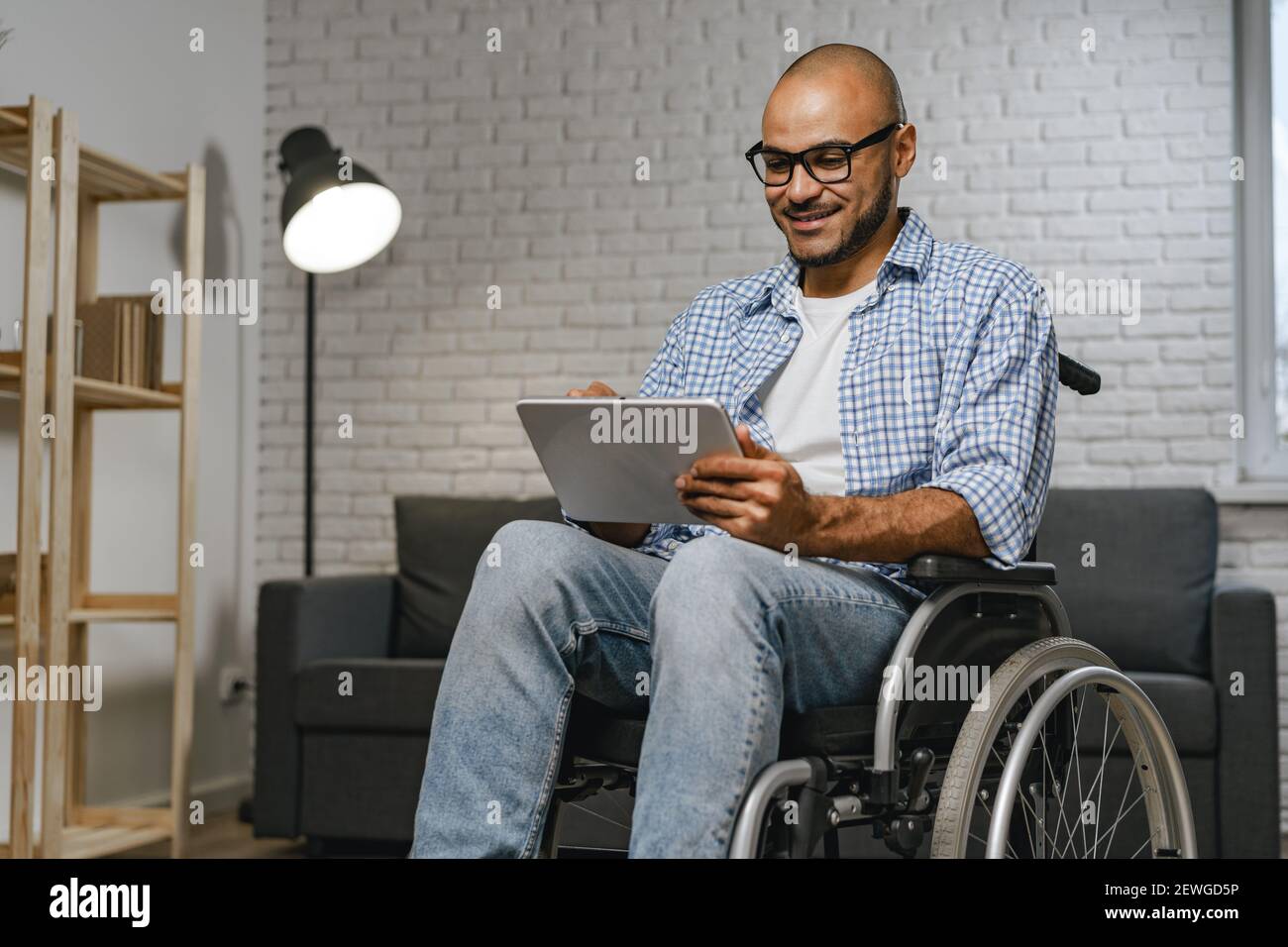 Behinderter junger afroamerikanischer Mann, der im Rollstuhl sitzt und benutzt Digitales Tablet Stockfoto