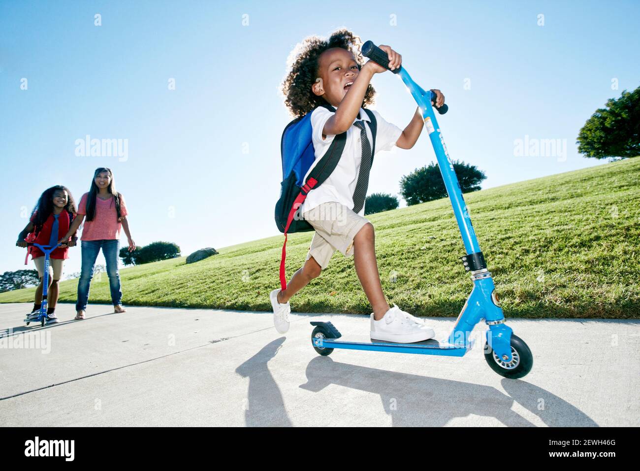 Sechsjähriger Junge auf einem Roller, gefolgt von seiner Schwester Stockfoto