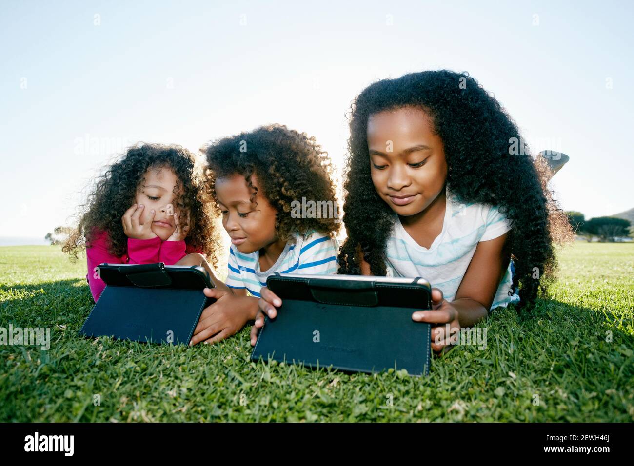 Junge gemischte Rennen Mädchen und ihr Bruder und Schwester liegen auf Gras mit zwei digitalen Tabletten, Bildschirm Zeit Stockfoto