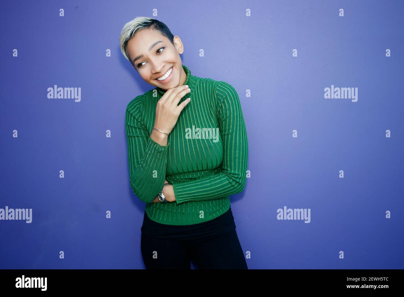 Eine junge schwarze Frau mit einem schüchternen Lächeln gegen ein Einfacher Hintergrund Stockfoto