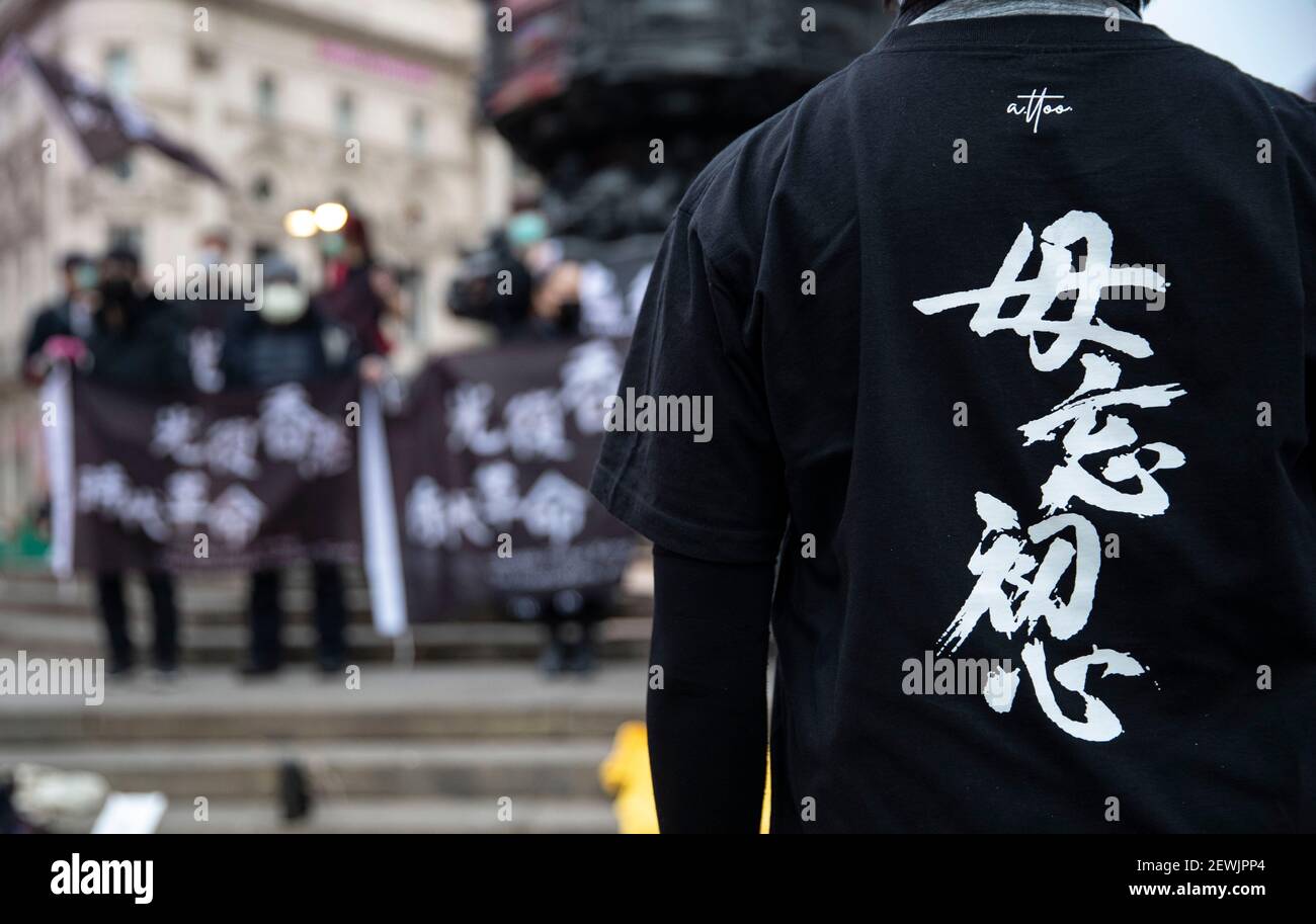 London, Großbritannien. März 2021, 1st. Ein Mann in einem T-Shirt mit der Aufschrift "Never forget why we Start" steht vor Anhängern, die eine verbotene Protestflagge mit der Aufschrift "Liberate Hong Kong, the Revolution of Our Times" am 01. März 2021 im Piccadilly Circus, London, Großbritannien, halten. Etwa 50 Unterstützer Hongkongs versammeln sich im Piccadilly Circus in London, um ihre Solidarität bei der Unterstützung der 47 prodemokratischen Aktivisten Hongkongs zum Ausdruck zu bringen, die im vergangenen Jahr bei den Primärwahlen helfen und die der Verschwörung zur Unterwanderung der Staatsmacht nach dem nationalen Sicherheitsgesetz beschuldigt werden, nehmen an ihrer ersten Gerichtsverhandlung Teil Stockfoto