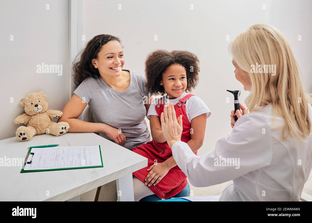 Hörkontrolle für ein Kind mit einem Otoskop. Afroamerikanisches Mädchen und ihre Mutter während eines Arztbesuchs Stockfoto