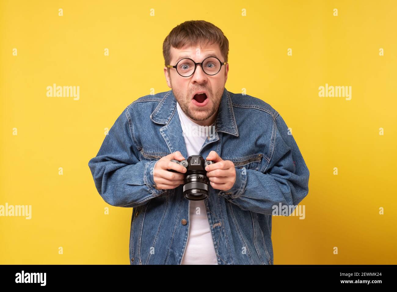 Studio-Porträt von goofy jungen Mann hält Fotokamera Aufnahme. Gelber Hintergrund. Stockfoto