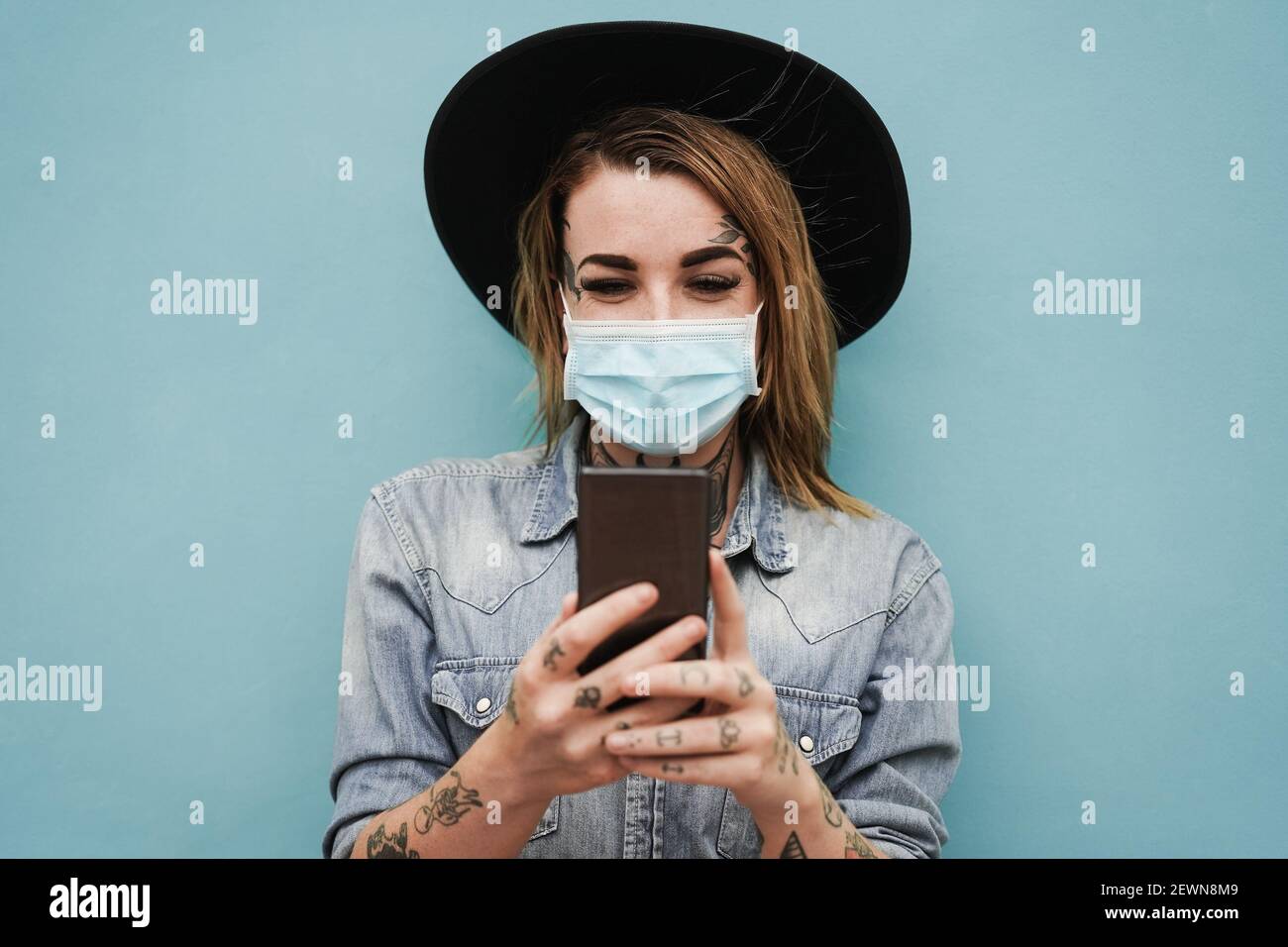 Junge Frau mit Tattoos mit Handy im Freien tragen Sicherheit Maske - Fokus auf Gesicht Stockfoto