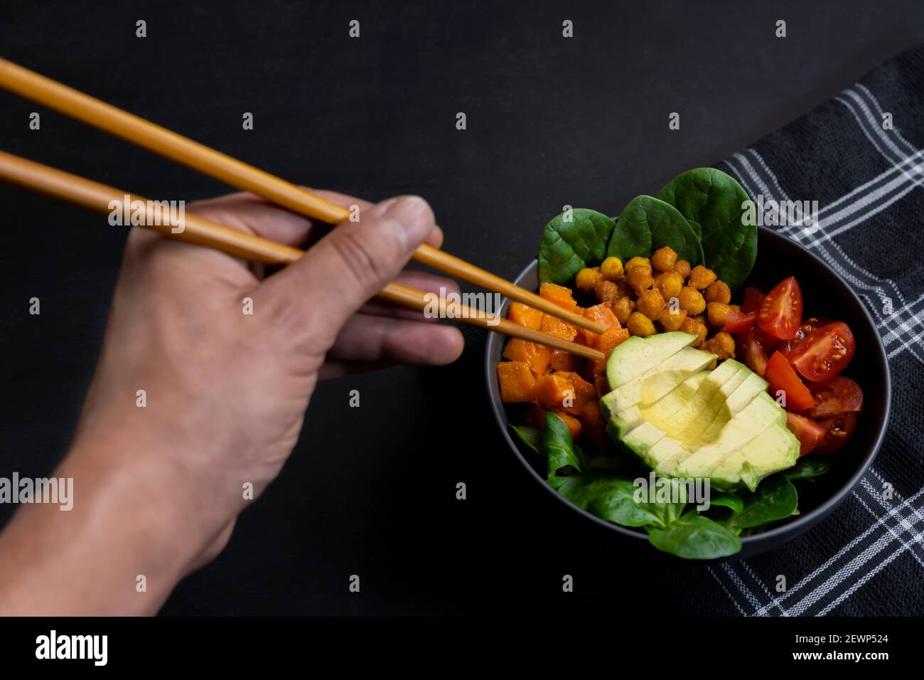 Essen vegetarische Poke Schüssel mit Essstäbchen auf dunklem Hintergrund.gesunde buddha Schüssel mit Avocado, Kirschtomaten, Spinat und Maissalat. Stockfoto