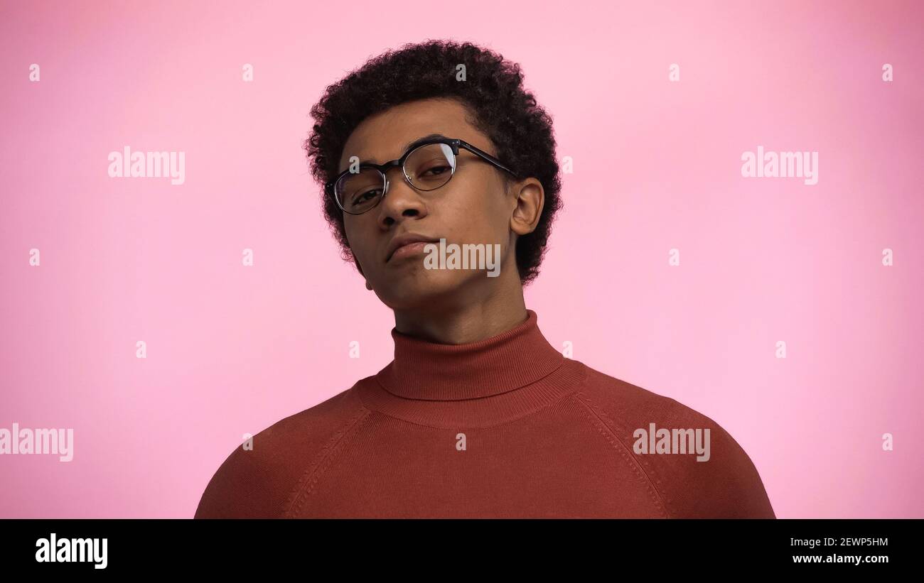 afroamerikanischer Teenager im Rollkragenpullover und Brille beim Betrachtend Kamera isoliert auf rosa Stockfoto