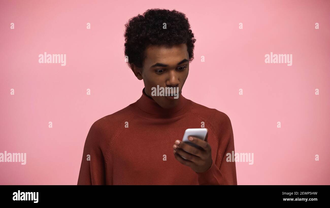 afroamerikanische Teenager in Rollkragen Pullover Blick auf Smartphone isoliert Auf Rosa Stockfoto