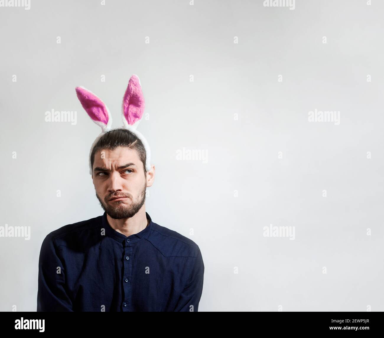 Kaukasischer Mann mit rosa Hasenohren ist in blauem stylischem Hemd gekleidet und sieht mit Vorsicht und Argwohn seitlich aus. Leerer Platz für Ihren Text oder Ihre Anzeige auf w Stockfoto
