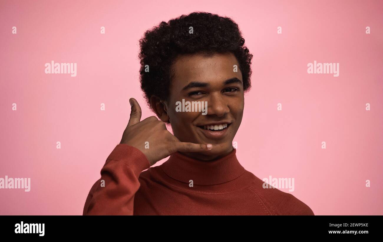 Happy african american Teenager junge im Rollkragenpullover zeigt Anruf Ich Geste isoliert auf rosa Stockfoto