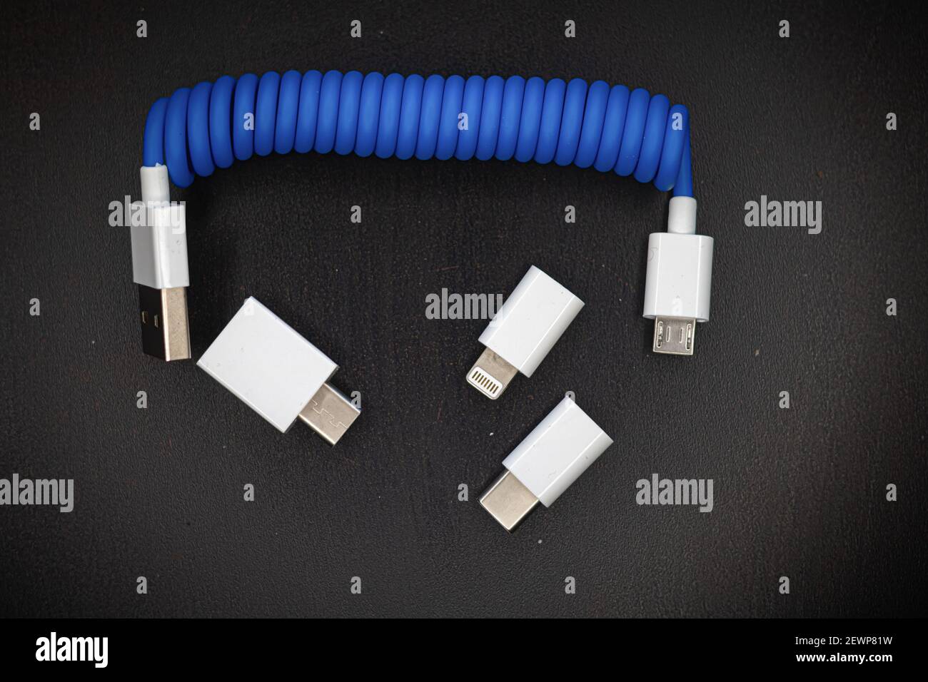 Blaues Spiral-USB-Kabel mit Adaptern für Micro, Mini-USB und Blitz isoliert auf dunklem Hintergrund Stockfoto