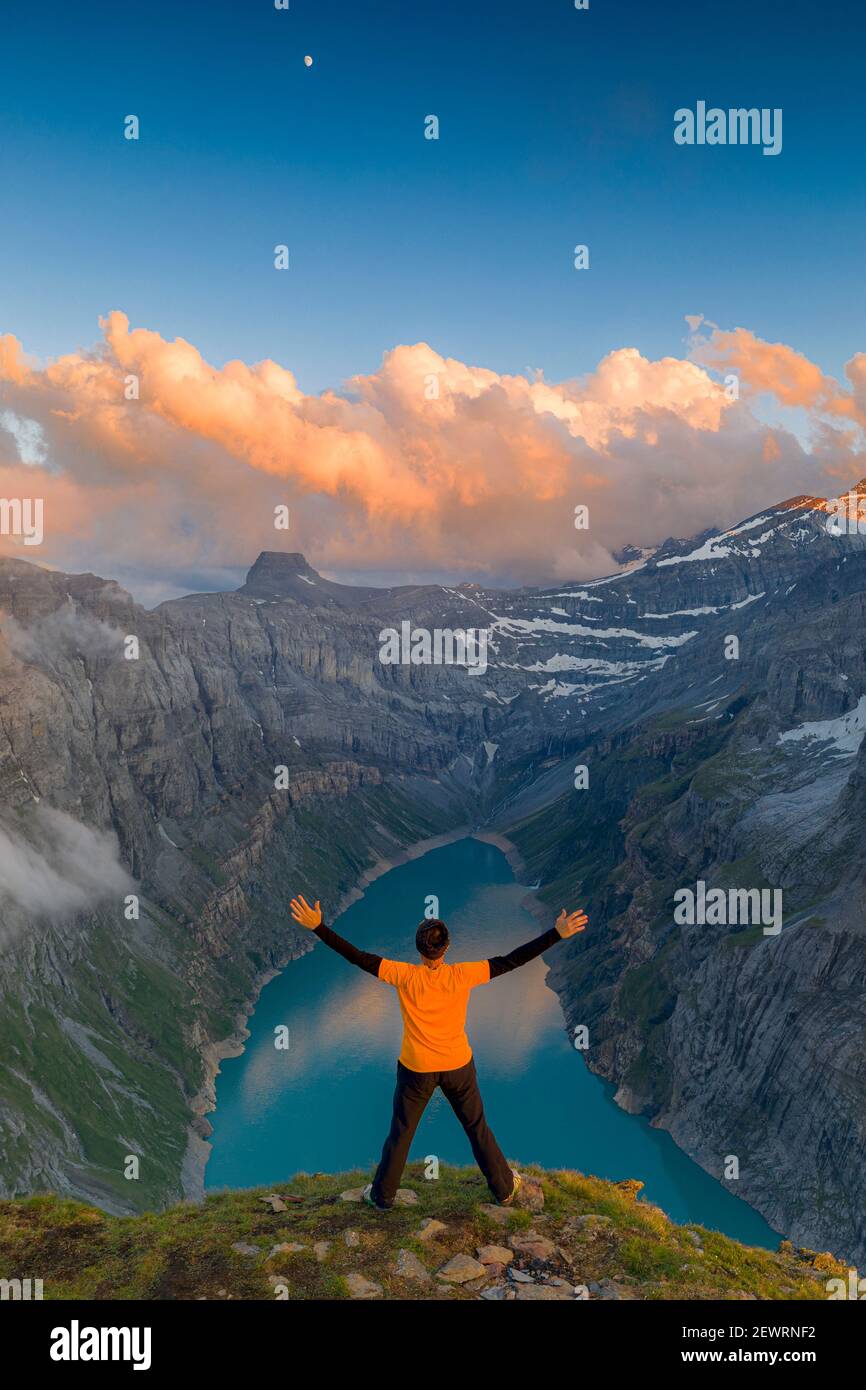 Mann mit ausgestreckten Armen, der den Sonnenuntergang über dem See Limmernsee genießt, der auf Felsen steht, Kanton Glarus, Schweiz, Europa Stockfoto