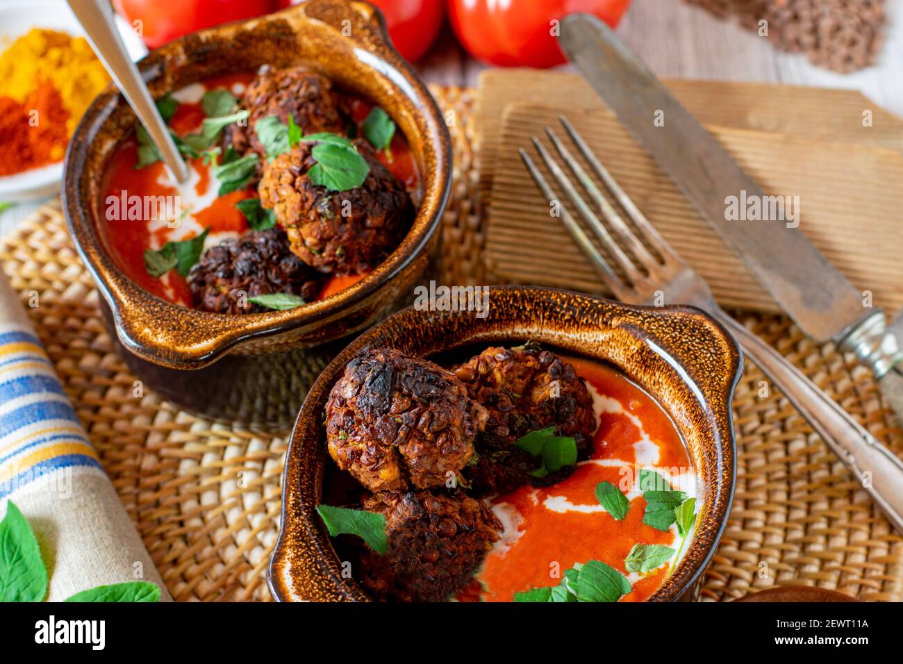 Veganes Gericht mit orientalisch würziger Tomatensuppe und Linsennüssen Fleischbällchen serviert in rustikalen braunen Schalen mit Kokosmilch gekrönt Stockfoto
