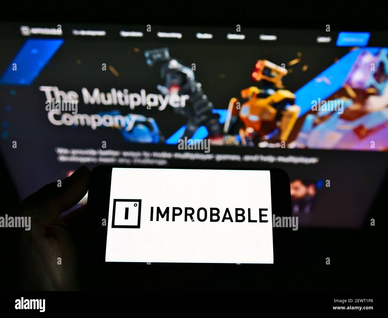 Person hält Handy mit Logo der britischen Software-Entwickler unwahrscheinlich Worlds Limited auf dem Bildschirm vor der Webseite. Konzentrieren Sie sich auf die Telefonanzeige. Stockfoto