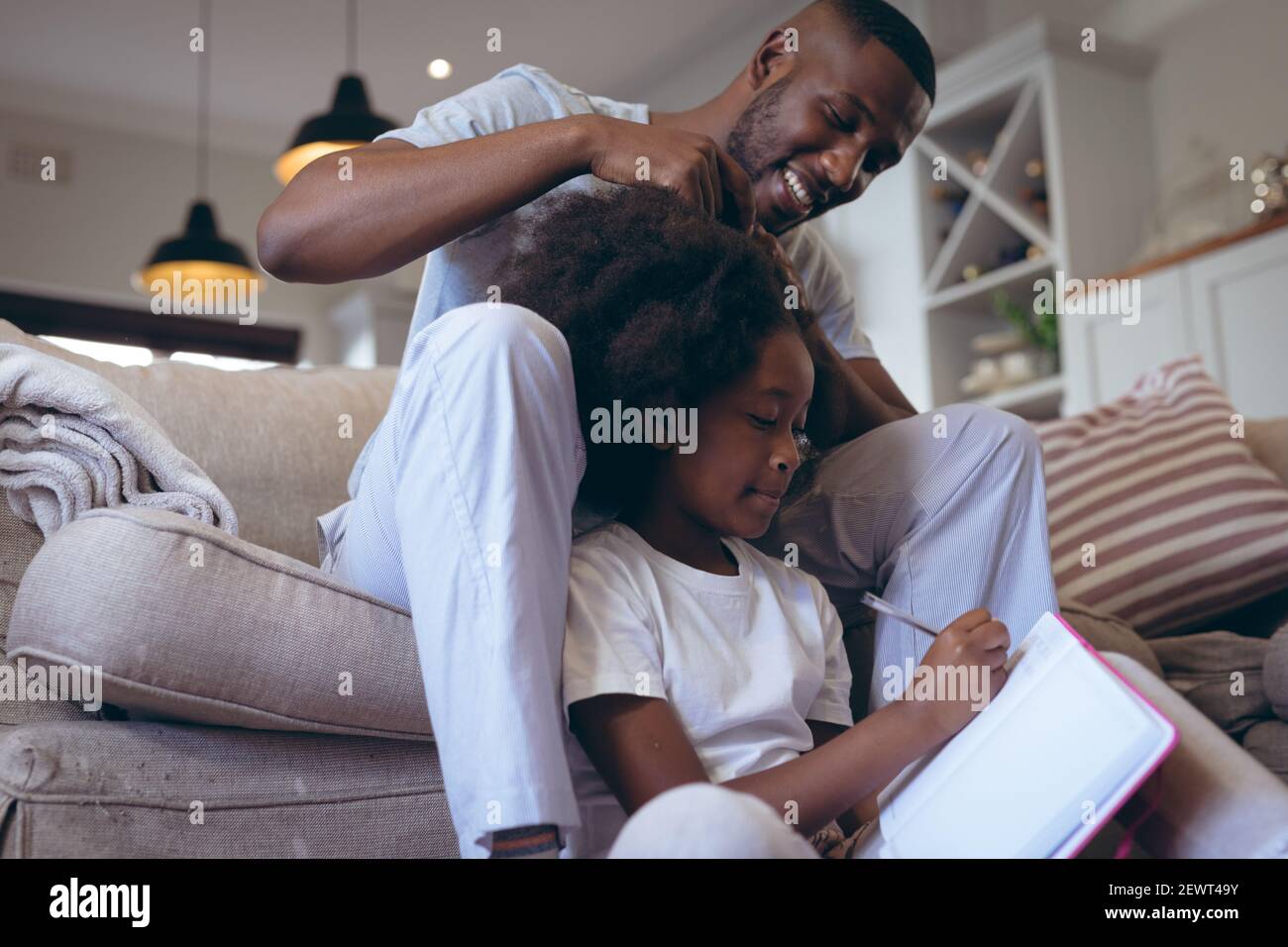 Afroamerikanischer Mann sitzt auf dem Bett und macht seine Tochter Haare Stockfoto