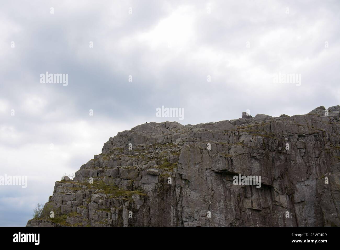 Schöne Details der zerklüfteten Felswand gegen den hellen bewölkten Himmel im Hintergrund bei Preikestolen in Norwegen. Stockfoto