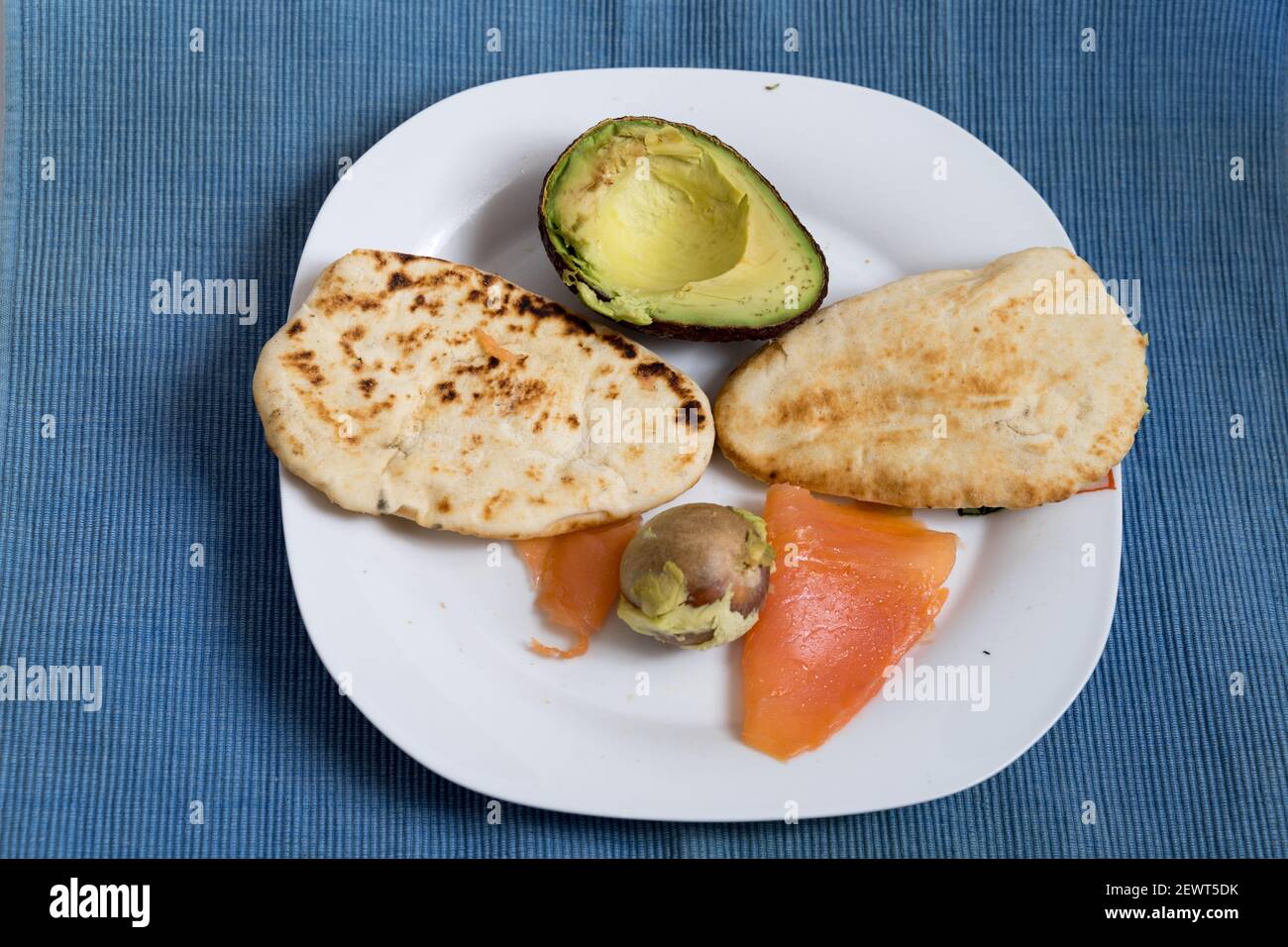 Zwei Naan-Brote, geröstet mit Lachs und halb Avocado Eine weiße Platte auf blauer Tischmatte Stockfoto