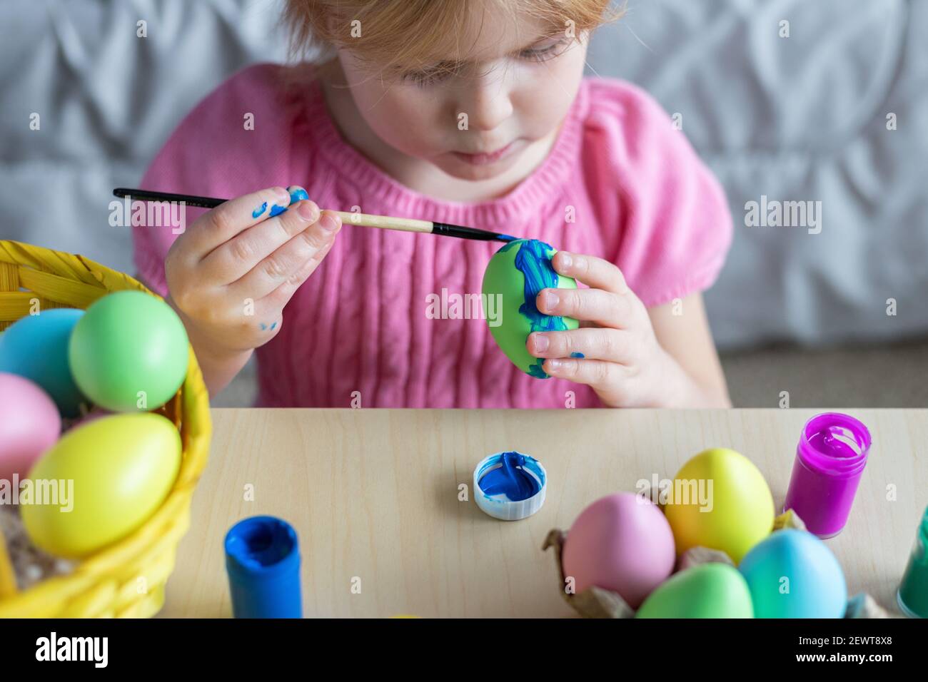 Kleines Mädchen in Osterhasen Ohren malen farbige Eier. Ostern Familienfeiertag zu Hause und Handwerk Konzept. Stockfoto