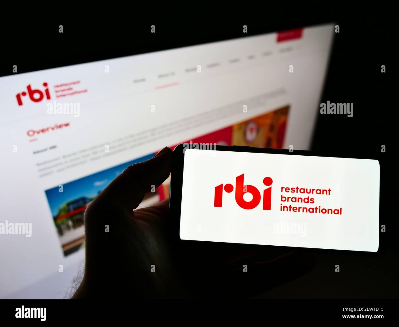 Person, die das Smartphone mit dem Logo des Lebensmittelunternehmens Restaurant Brands International Inc. (RBI) auf dem Bildschirm vor der Website hält. Konzentrieren Sie sich auf die Telefonanzeige. Stockfoto