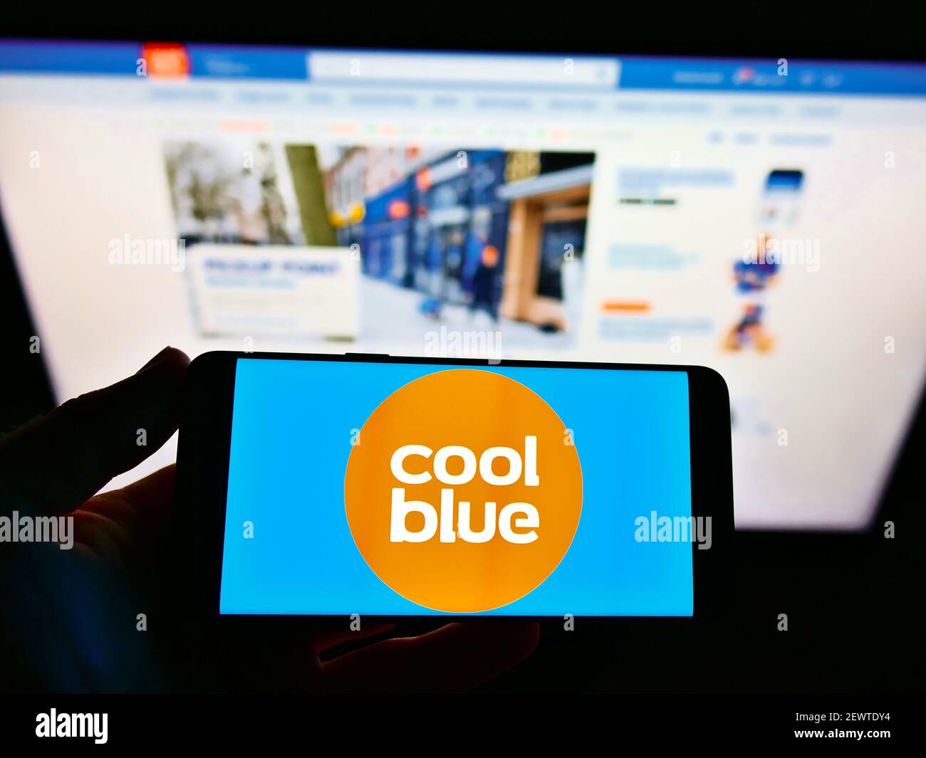 Person hält Smartphone mit Logo des niederländischen Online-Shop-Unternehmen coolblue BV auf dem Bildschirm vor der Business-Webseite. Fokus auf Handy-Display. Stockfoto