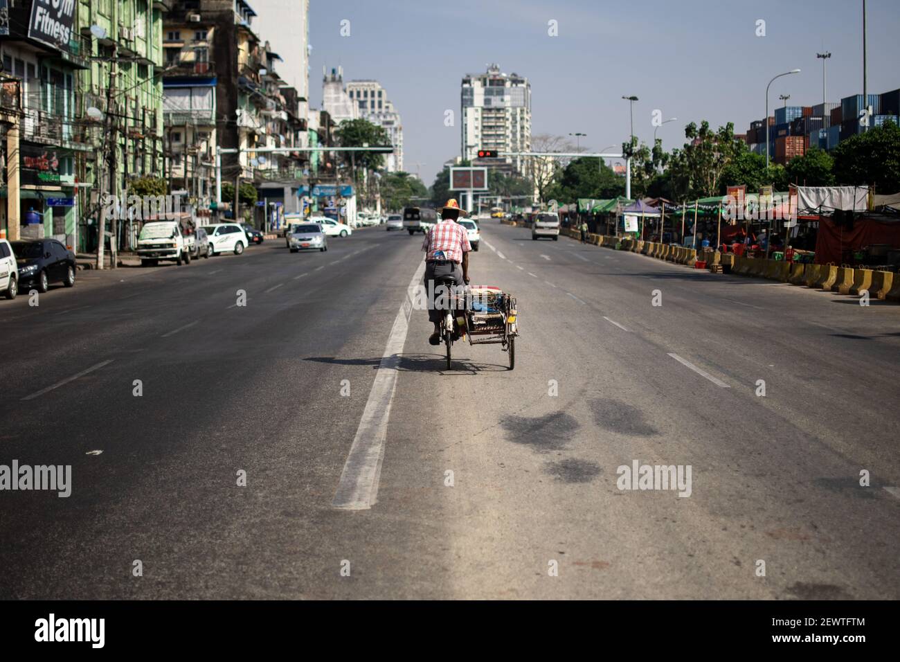 YANGON, MYANMAR - JANUAR 1 2020: Ein burmesischer Mann im traditionellen Longyi fährt an einem warmen Tag mit dem Fahrrad mitten auf der Straße im Verkehr Stockfoto
