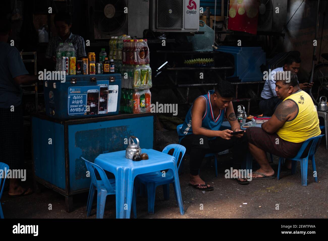 YANGON, MYANMAR - JANUAR 1 2020: Ein paar Burmesen sitzen auf Plastikstühlen und ruhen sich an einem Imbiss- und Getränkestand in der Innenstadt aus Stockfoto