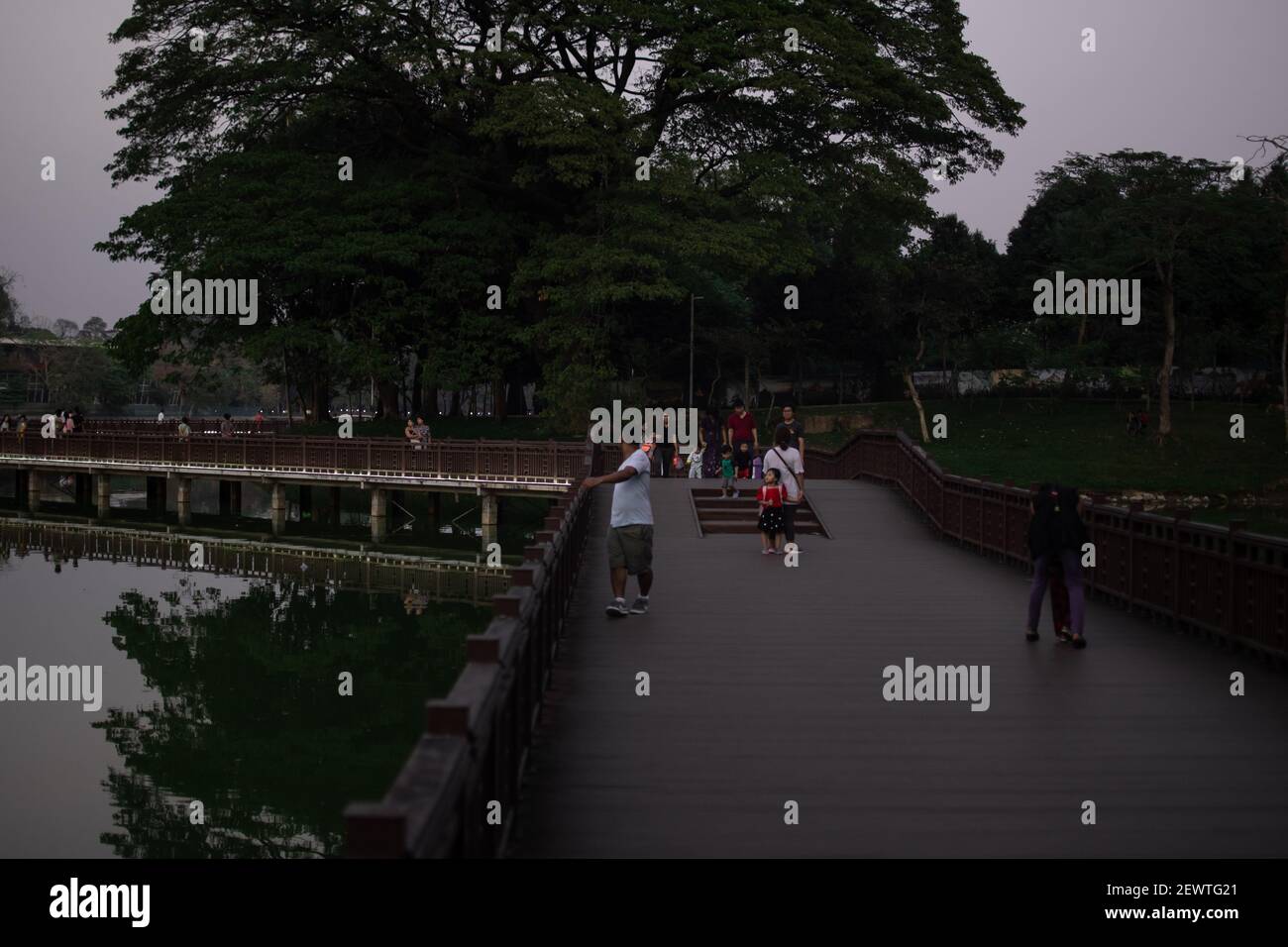 YANGON, MYANMAR - JANUAR 1 2020: Die Menschen besuchen den Kandawgyi Park und wandern am Abend entlang der Wegbrücke um den See Stockfoto