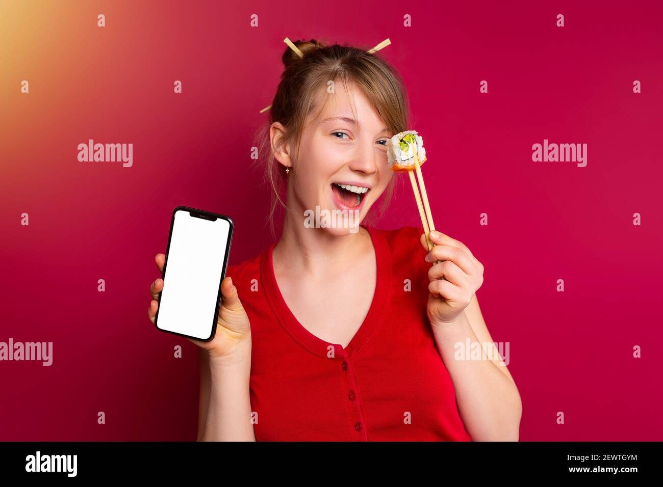 Stilvolle blonde Mädchen Abdeckung Auge kalifornien Sushi-Rolle, rot Studio Hintergrund mit Platz für Werbung. Ziemlich weiblich hält japanisch Rolle durch Stockfoto