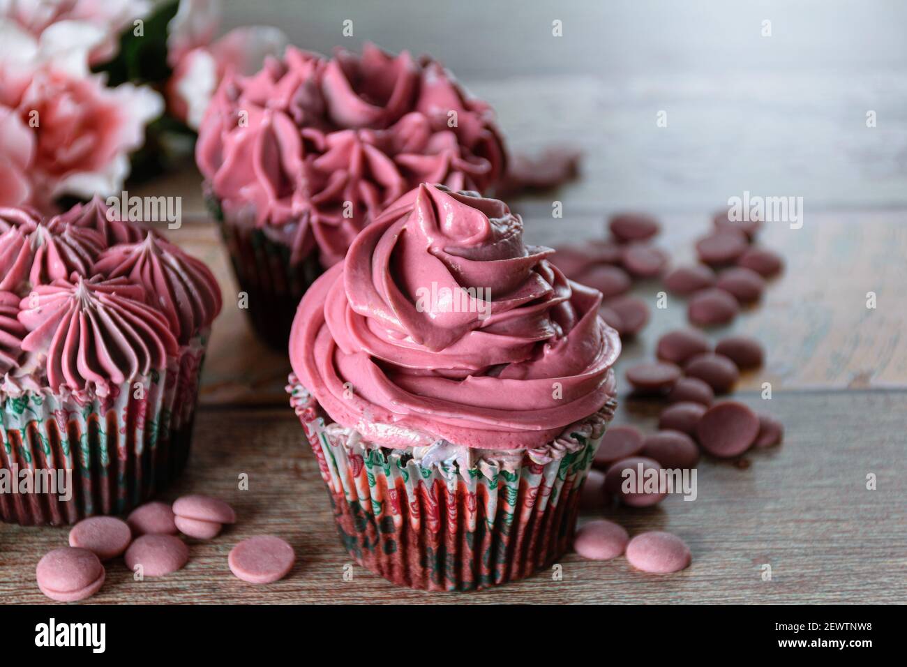 Nahaufnahme von drei Schokoladen-Cupcakes mit rosa Buttercreme. Neben Rubinschokolade-Callets (mit Kopierraum). Stockfoto