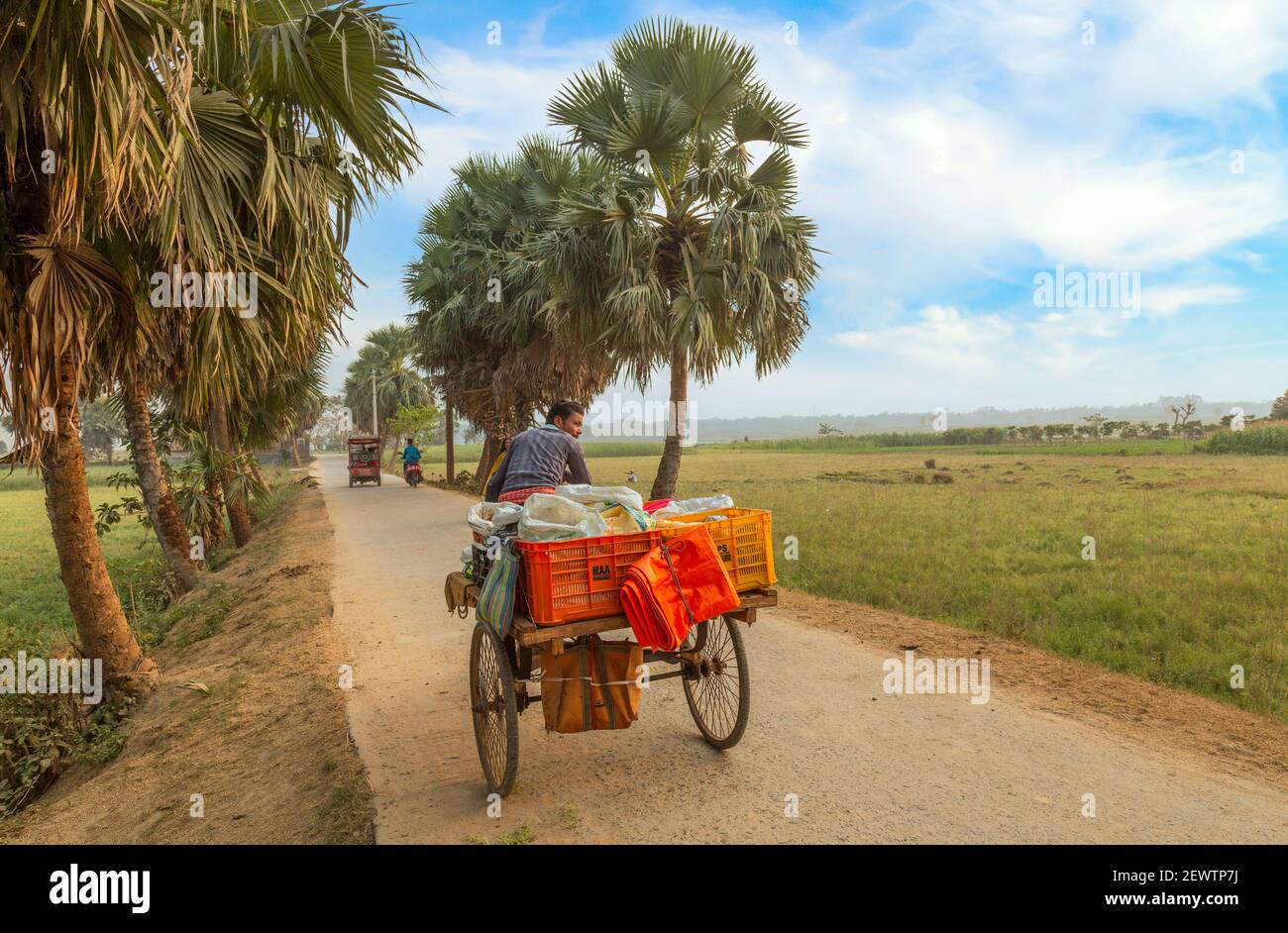 Der Mensch auf seinem Fahrradwagen, der notwendige Waren auf einem verkauft Dorfstraße mit Blick auf ländliche Landschaft bei einem Bezirk In Westbengalen Indien Stockfoto