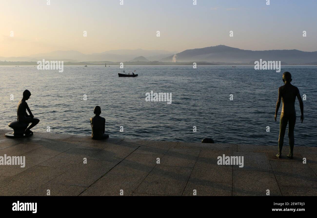 Die berühmte Raqueros Bronzeskulptur von verwaisten Jungen Santander Bucht Kantabrien Spanien an einem sonnigen Wintermorgen mit kleinen Fischen Boote und Berge Stockfoto