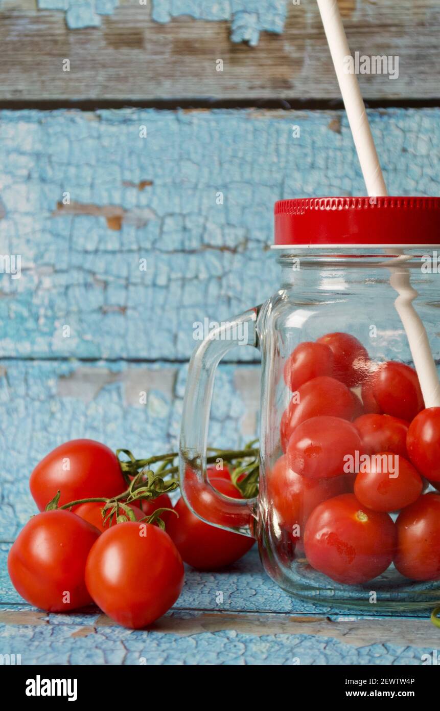 Viele kleine Tomaten in einem Glas mit rotem Deckel Vor blauem Hintergrund in Nahaufnahme Stockfoto