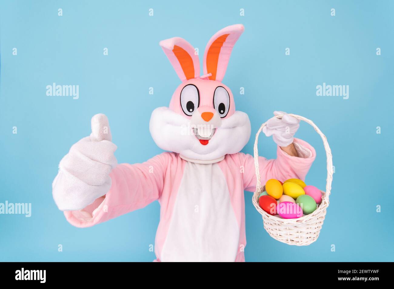 Frohe Ostern. Osterhase oder Kaninchen oder Hase hält Ei mit Korb von farbigen Eiern, Spaß haben, feiert Osterhase isoliert auf blauem Hintergrund. Stockfoto